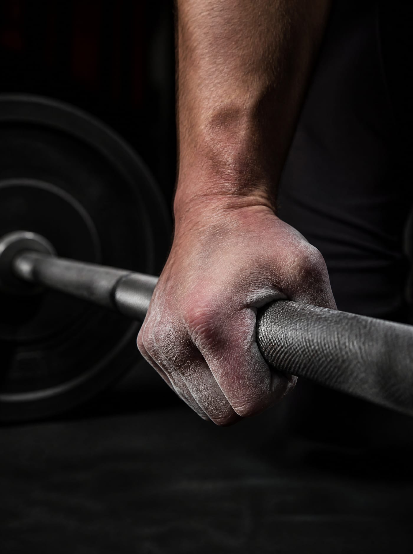 Main couverte de craie serrant une barre olympique moletée dans une salle sombre